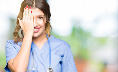 Poster - Young adult doctor woman wearing medical uniform covering one eye with hand with confident smile on face and surprise emotion.