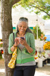 © ML Harris - Happy, mature, black, African American woman texting with  cell phone at farmers market. Seniors using mobile technology.