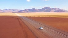 High Aerial Over A Toyota Safari Vehicle Heading Across The Flat, Barren Namib Desert In Namibia.