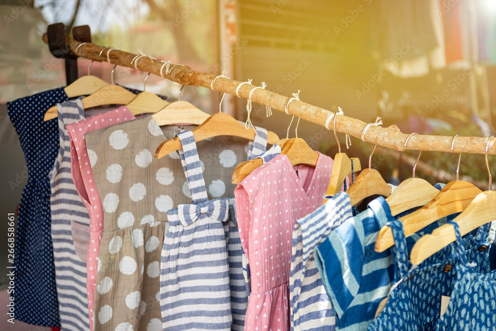 Kids's fashion, cute little girl dress hanging on wooden stick over blurred cloth shop background - obrazy, fototapety, plakaty 