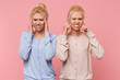 © timtimphoto - Beautiful young blonde twins experience discomfort, pain in temples and tinnitus isolated over pink background.