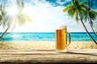 Summer background of wooden desk and cold beer. Free space for your decoration. Beach landscape with palms and ocean. Summer sunny day with sun light. Beach party and summer time. 