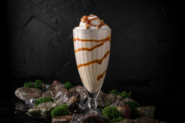 Milkshake. Cold drink of milk, ice cream, chocolate and caramel on a black background with stones and ice. Cocktail card for a bar or restaurant.