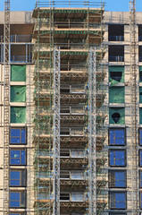 Wall Mural - tall modern multistory apartment building under construction with scaffolding and hoist frames under a blue sky