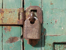 Close Up Of An Old Rusted Metal Padlock Fastening An Iron Bar On A Green Wooden Door