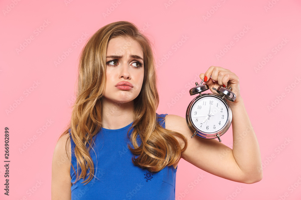 Displeased young pretty woman posing isolated over pink wall background holding alarm clock. - obrazy, fototapety, plakaty 