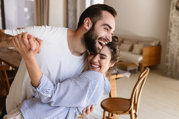 Wall Mural - photo of laughing brunette couple in love smiling while hugging together in apartment