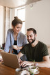 © Drobot Dean - Image of pleased brunette couple working on laptop together while sitting at table at home