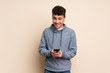 © luismolinero - Young man over isolated wall sending a message with the mobile