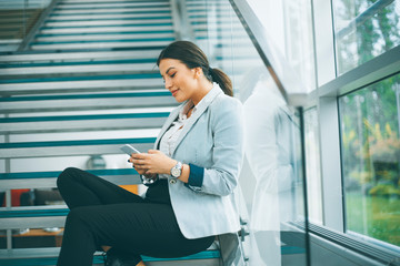 Young business woman sitting on the stairs at the office and use mobile phone