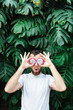 Young bearded man holding slices of Pitaya dragon fruit in front of his eyes, surprised