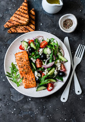 Wall Mural - Healthy balanced lunch - grilled red fish fillet salmon and vegetables, olives, feta salad on dark background, top view