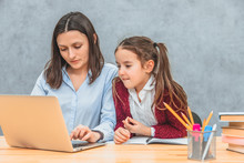 A Young Mother And A Schoolgirl Look In A Gray Laptop. On A Gray Background. The Wife Is Typing Word On The Laptop.