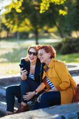 Wall Mural - Mother and daughter in the park sharing content on their smartphones