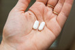 Close-up view of a hand holding two white pills in the palm above a blurry background, painkiller