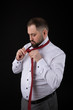 © Volodymyr Shcherbak - Elegant businessman in a white shirt, straightens ties his tie ob black background
