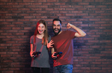 Wall Mural - Young man and teenage girl playing video games with controllers near brick wall