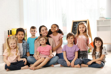 Sticker - Group of cute little children with teacher sitting on floor in kindergarten