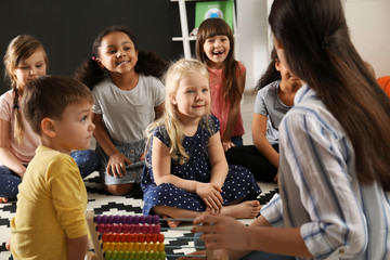 Sticker - Cute little children with nursery teacher in kindergarten. Indoor activity