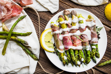 Fresh cooked green asparagus with ham and sauce on plate, top view