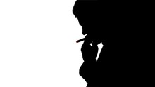 Silhouette Of Smoking Man With Burning Cigarette.Silhouette Of A Man Smoking A Cigarette. He Takes A Drag, Then Lets Out A Puff Of Smoke That Slowly Dissipates. He Is Contemplating His Life Choices An