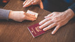 © Alina Rosanova - Male and female hands on table exchange Italian passport and money - concept of illegal immigration, sale of fake passports, sham (fake) marriage