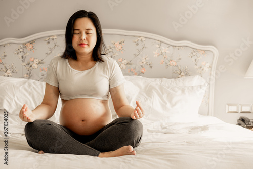 Pregnant Woman Doing Yoga Exercise On Bed In Bedroom At Home