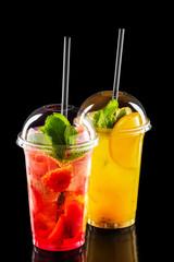 Two take away glasses with strawberry and orange lemonade isolated on black