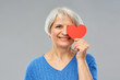 © Syda Productions - valentine's day, summer and old people concept - portrait of smiling senior woman covering one eye with red heart over grey background