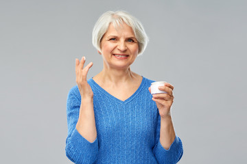 Wall Mural - beauty, old age and cosmetics concept - smiling senior woman with jar of face cream over grey background