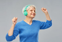 Technology And Old People Concept - Smiling Senior Woman In Glasses And Headphones Listening To Music Over Grey Background