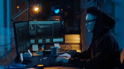 cybercrime, hacking and technology concept - asian male hacker in glasses writing code or using computer virus program for cyber attack and drinking coffee in dark room at night