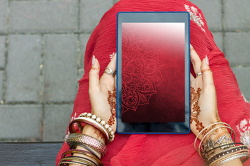 Wall Mural - Beautiful woman wear traditional Muslim Arabic Indian wedding red pink sari dress hands with henna tattoo mehndi pattern jewelry and bracelets hold tablet. Summer culture festival celebration concept.