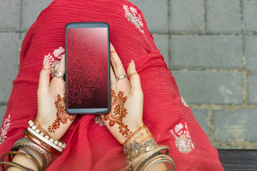 Wall Mural - Beautiful woman wear traditional Muslim Indian wedding red pink sari dress hands with henna tattoo mehndi pattern jewelry and bracelets hold smartphone. Summer culture festival celebration concept