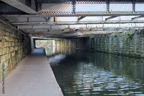 Fotografía view under an old low steel girder bridge crossing the leeds to liverpool canal