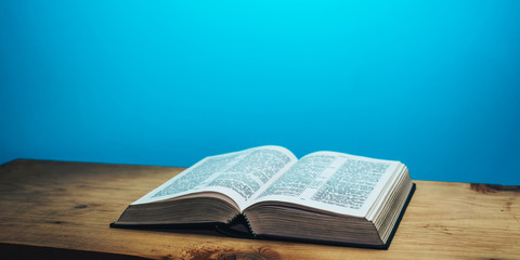 Bible on a brown wooden table. Beutiful blue wall background.