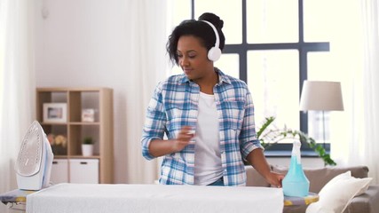 Sticker - people, housework, laundry and housekeeping concept - happy african american woman in headphones ironing bed linen on board and dancing at home