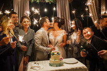 Young Beautiful Wedding Couple Cut Wedding Cake With Friends And Have Fun With Bengal Lights