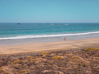 Wall Mural - People walking on the Famara seafront, beach and mountains overlooking the ocean. Lanzarote, Canary Islands, Spain. Africa