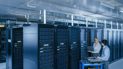 In the Modern Data Center: Engineer and IT Specialist Work with Server Racks, on a Pushcart Equipment for Installing New Hardware. Specialists Doing Maintenance and Diagnostics of the Database.