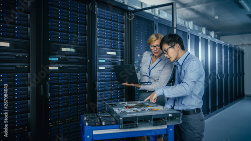 In the Modern Data Center: Engineer and IT Specialist Work with Server Racks, on a Pushcart Equipment for Installing New Hardware. Specialists Doing Maintenance and Diagnostics of the Database.