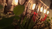 Christmas Interior Decoration: Modern Iron Scones With Incandescent Lamps And Huge Red Textile Bows Shine Bright On Shell Rock Wall. Home Plants With Green Leaves And Bottles Wine In Warm Atmosphere.