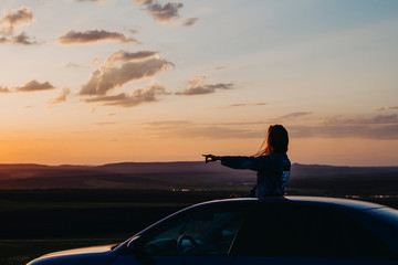 Silhouette of a woman at sunset who travels by car, a woman looks out of the car and shows her hand to the side