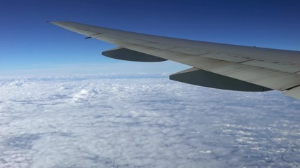 Wall Mural - 4K, Beautiful clouds from above, as seen through airplane window. Traveling by air. View of traveler in cabin at turbine and plane wing in flight trip with beautiful blue sky. -Dan