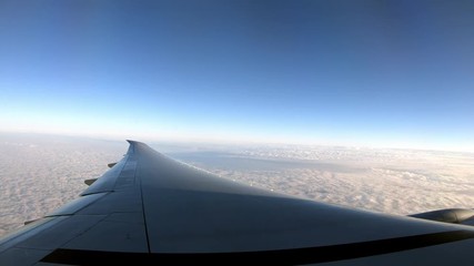 Wall Mural - 4K, Beautiful clouds from above, as seen through airplane window. Traveling by air. View of traveler in cabin at turbine and plane wing in flight trip with beautiful blue sky. -Dan