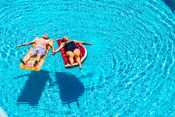 Total relax for happy mature senior retired people lay down on coloured lilos inflatable mattress on blue clear water of swimming pool in summer time - enjoying lifestyle and vacation