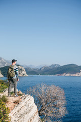 Wall Mural - A tourist with a backpack on top of a cliff or hill next to the sea looks into the distance. Travel alone.