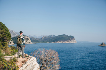 Wall Mural - A tourist with a backpack on top of a cliff or hill next to the sea looks into the distance. Travel alone.