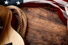 American Culture, Living On A Ranch And Country Muisc Concept Theme With A Cowboy Hat, USA Flag, Rope Lasso And Acoustic Guitar On A Wooden Background In A Old Saloon With Copy Space