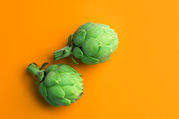 Ripe green artichokes on bright solid orange background. Creative food poster. Minimalist style. Mediterranean Spanish cuisine healthy plant based diet superfoods concept